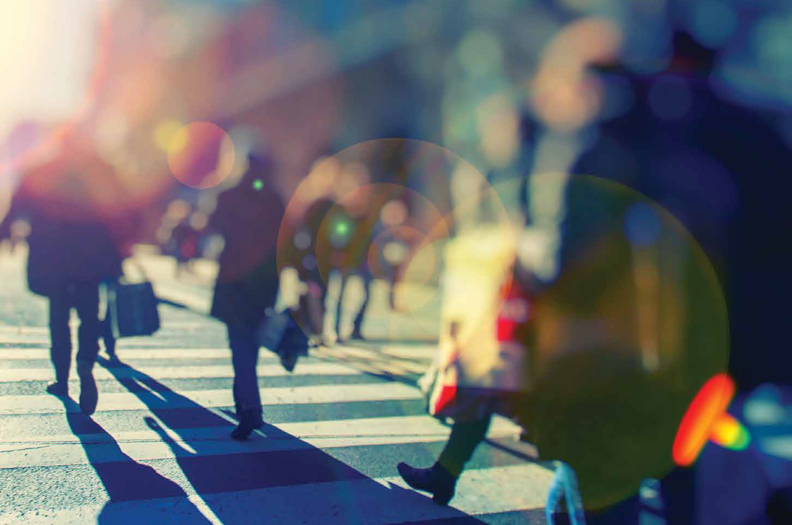 High-contrast, partly blurred image of people walking across a zebra crossing with colourful lens flare