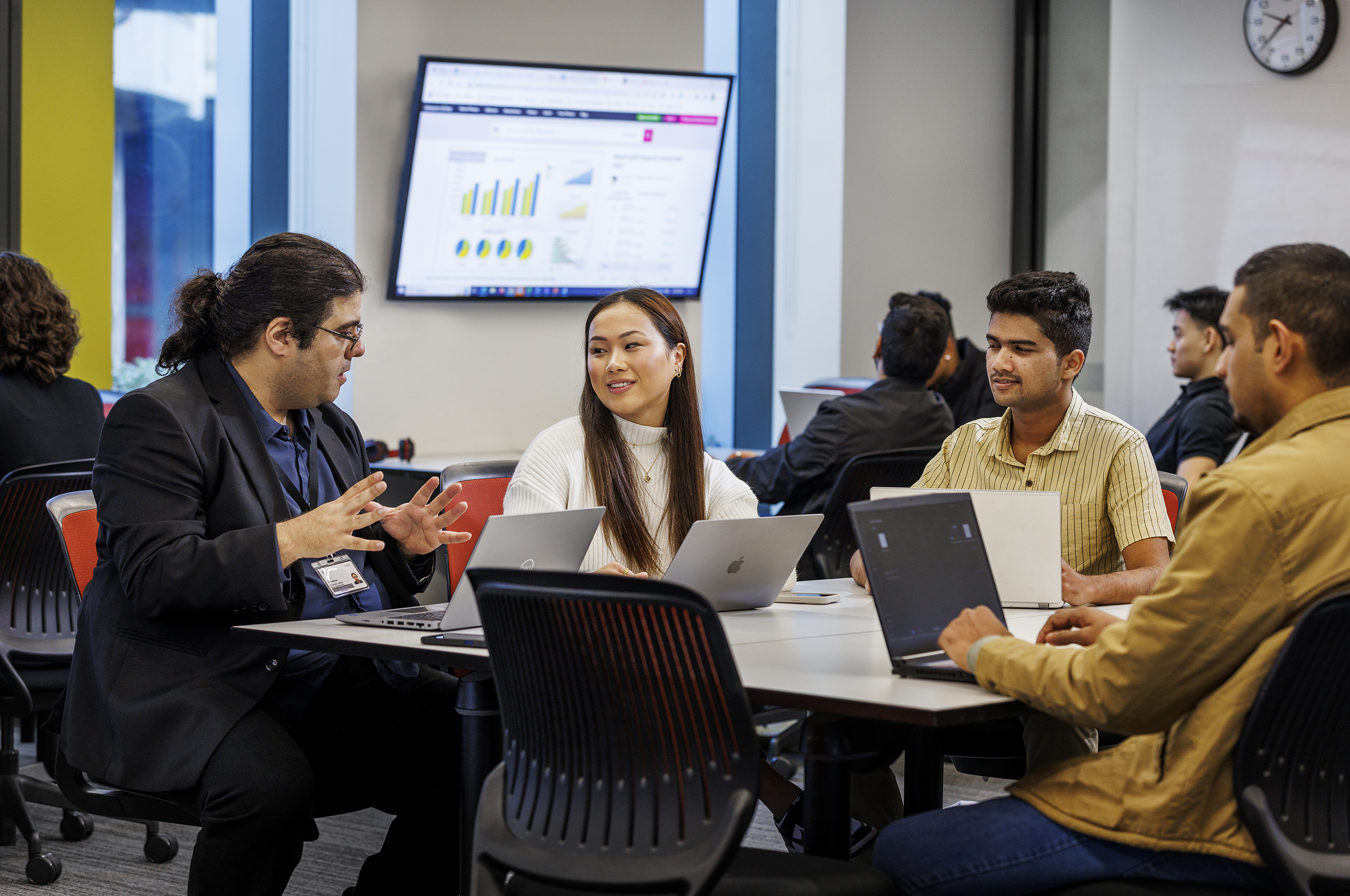 A La Trobe tutor speaking to students sitting at a table in a classroom.