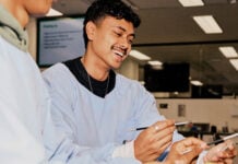 La Trobe biomed student in scrubs standing next to other student and smiling while holding medical device