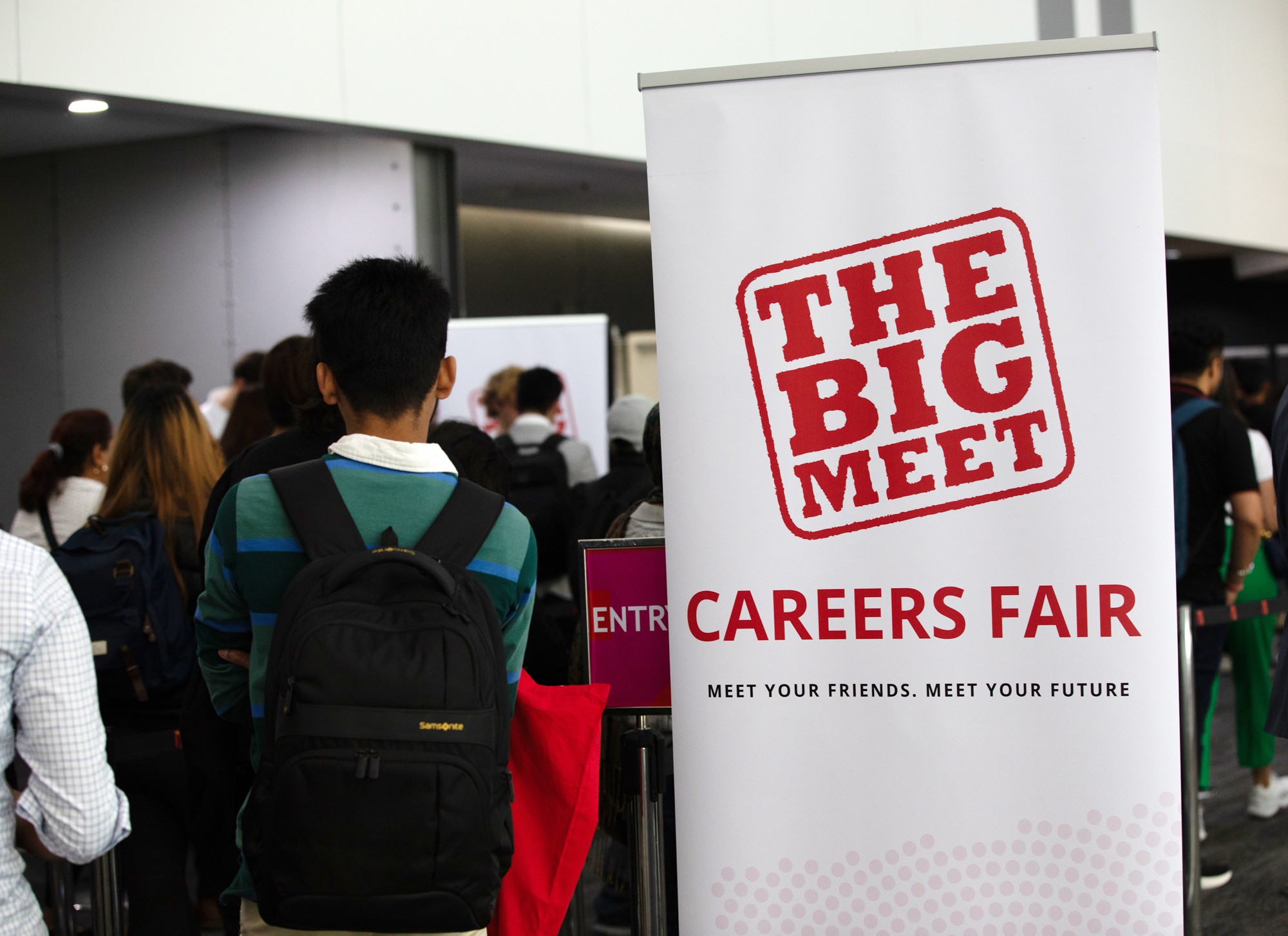 Student walking into Big Meet event standing next to a banner with the words 'The Big Meet Careers Fair' displayed