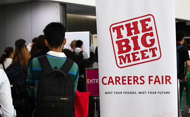 Student walking into Big Meet event standing next to a banner with the words 'The Big Meet Careers Fair' displayed