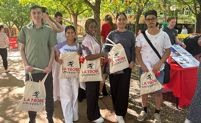 Students posing for a photo at O Week holding La Trobe branded tote bags