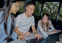 Students gathered around a laptop looking at the screen and smiling