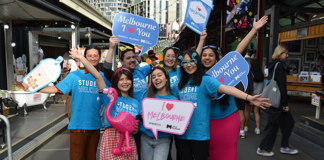 Students wearing blue t shirts happily posing for a photo in the City of Melbourne