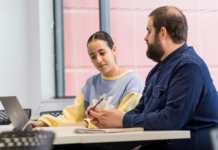 Two students sitting at a table looking at laptop