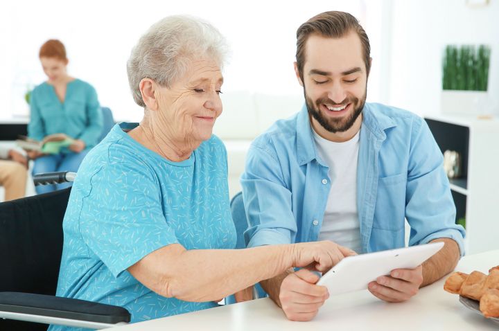 Older woman and younger man sitting together looking at an iPad.